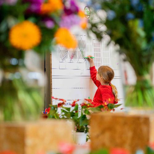 beeld van jong meisje dat op bord tekent omringd door bloemen buiten focus